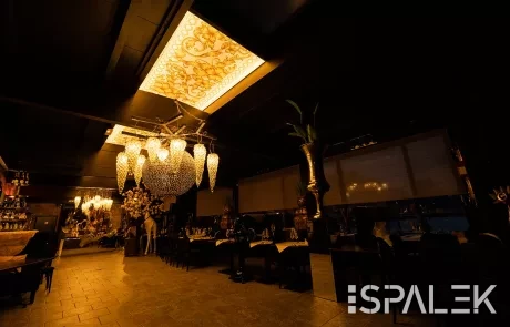 Elegantes, schummrig beleuchtetes Restaurant mit verzierten Kronleuchtern, goldenen Deckenelementen, dunklem Mobiliar und gedeckten Tischen.