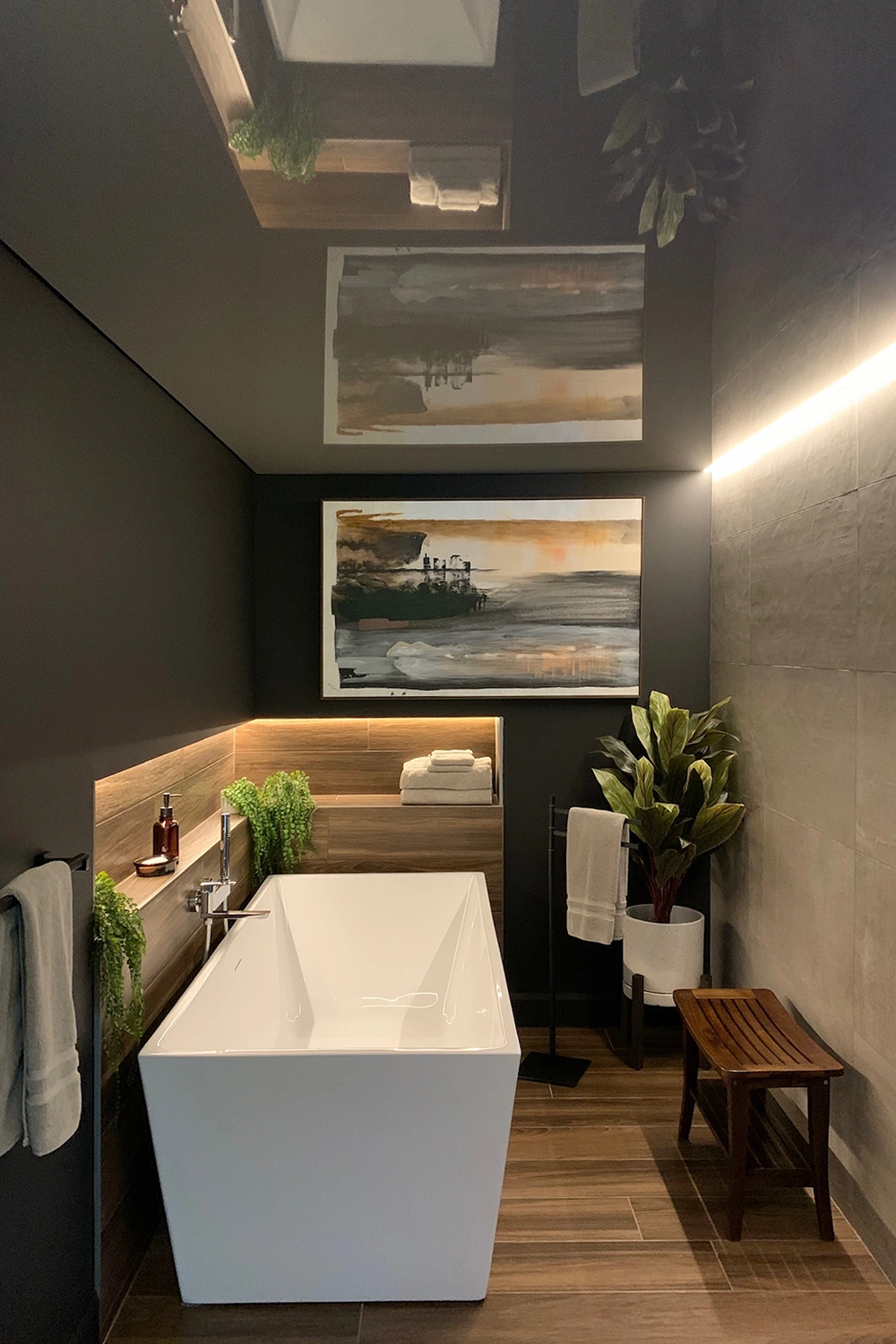 Bad-hochformat Modernes Bad mit weißer Quadrat-Badewanne, dunklen Wänden, Holzfußboden, Akustikdecke, großem Bild und warmer Beleuchtung.