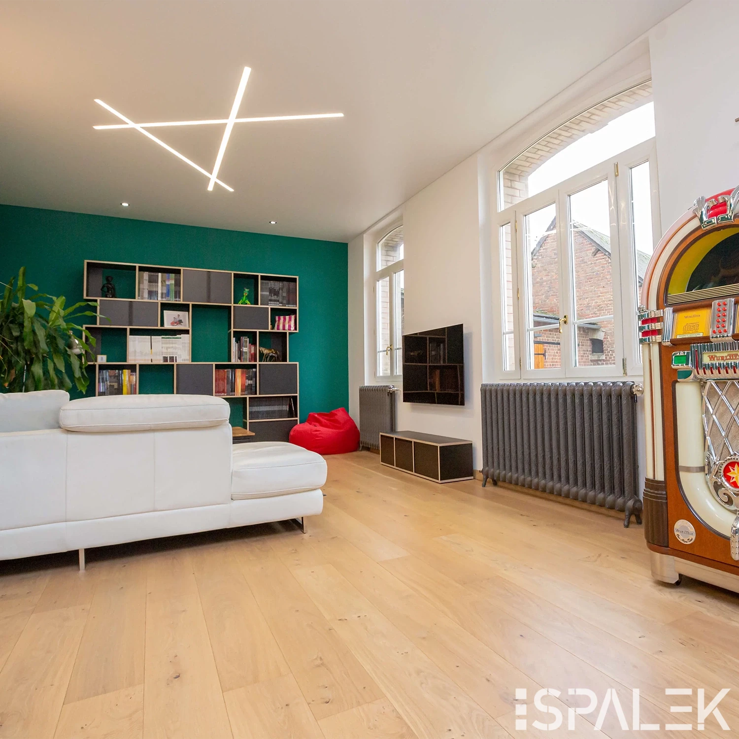 Modernes Wohnzimmer mit weißem Ecksofa, Holzboden, Akustikdecke, grüner Akzentwand, Wandregalen, TV und großem Fenster.