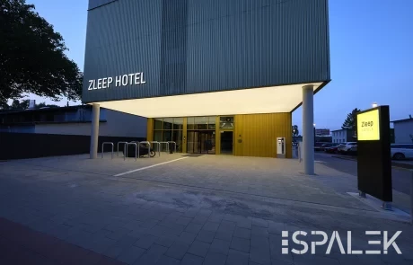 Moderner Hoteleingang in der Dämmerung mit beleuchtetem Zleep Hotel Hamburg Schild, Glas-Eingangstür, Fahrradständern und Vordach.
