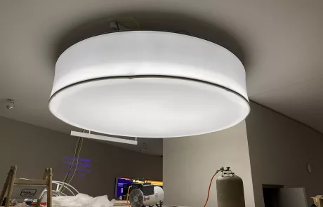 Ein großer, runder Deckenleuchtkörper hängt über einem Arbeitstisch mit Werkzeugen und Geräten in einem Rohbau des Museums Sensoria.
