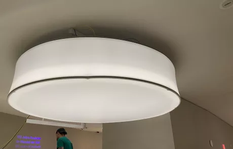 Große, runde Deckenleuchte an der Decke. Darunter im Museum Sensoria steht eine Person nahe einer bunt projizierten Wand.