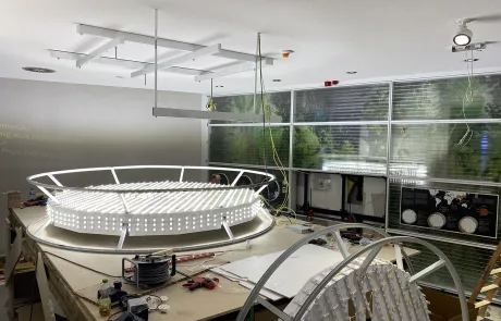 Eine große, runde LED-Leuchte wird auf einer Werkbank in einem modernen Raum des Museum Sensoria, Holzminden montiert.