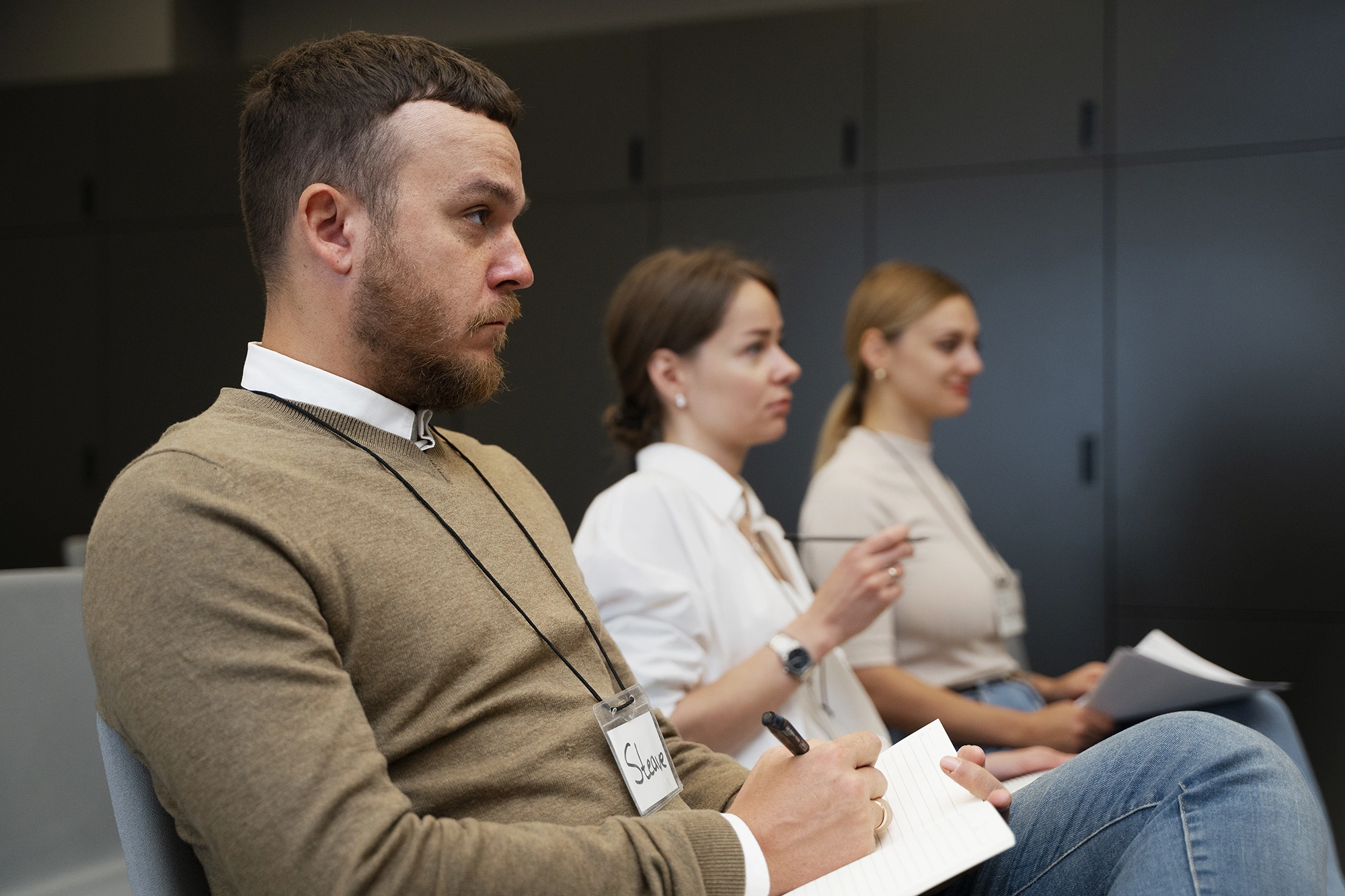 Akustikseminar Drei Personen sitzen unter Akustikdecken in einem Raum, machen sich Notizen und blicken aufmerksam auf etwas außerhalb des Bildes.