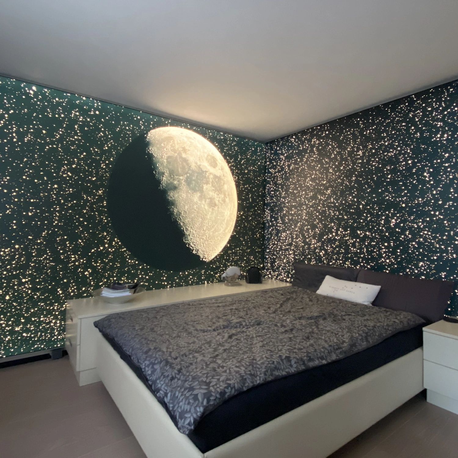 Gemütliches Schlafzimmer mit großem Bett, Wänden mit kleinen, sternförmigen Lichtern und leuchtendem Halbmond über dem Nachttisch.