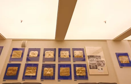 Lichtburg4 Wandpräsentation mit zwölf goldfarbenen Tafeln auf blauem Grund, Infotafel und Fotos rechts, unter heller Decke in der Lichtburg Essen.