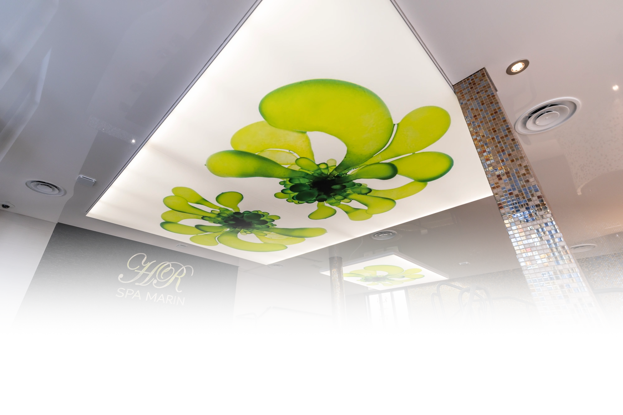 Decke mit großen, abstrakten grünen Blumendesigns über modernem Spa mit Mosaiksäulen, Metallgeländern und goldener Wandaufschrift.