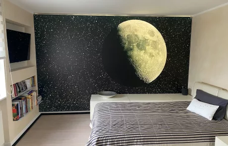 SchlafzNachher Modernes Schlafzimmer mit gestreiftem Bett, Bücherregalen und großer Wandgestaltung mit detaillischem Mond vor Sternenhimmel.