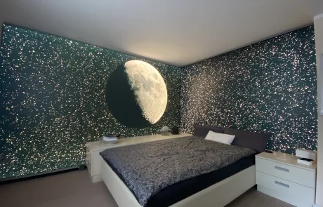 Schlafzkomplett Modernes Schlafzimmer mit dunkelgrünen Wänden, kleinen weißen Lichtern und großem Mondmotiv über einem Bett mit grauer Bettwäsche.