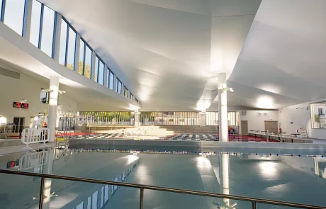 HD-9187-R Ein Hallenbad im Centre Aquatique de Viroflay mit klarer Wasseroberfläche, weißen Wänden, großen Fenstern und modernen Deckenleuchten.