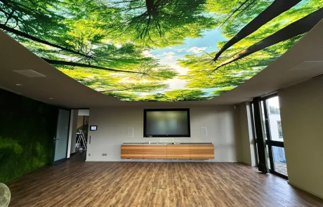 Moderner Besprechungsraum mit Holzfußboden, großen Fenstern und einer Decke mit Fotomotiv von Baumkronen und Himmel.