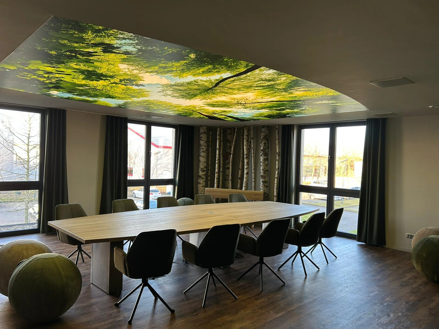 Moderner Westpress Besprechungsraum mit großen Fenstern, langem Holztisch, schwarzen Stühlen, grünen Sitzbällen und Baumdeckenmotiv.