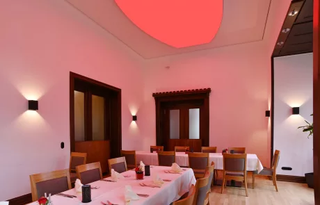 IMG_1389 Esszimmer in Hirschburg mit zwei gedeckten Tischen, Holzstühlen, rosa Wänden und leuchtender Decke in gemütlicher Atmosphäre.