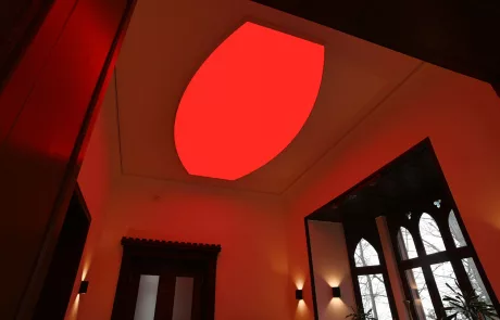 IMG_1391 Moderne Decke mit großem, leuchtend rotem ovalem Lichtpanel bei Vodafone Deutschland, rote Lichtreflexe auf cremefarbenen Wänden.