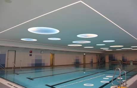 Hallenbad Erolzheim mit klarem blauen Wasser, gefliestem Beckenrand und moderner Decke mit runden Oberlichtern.