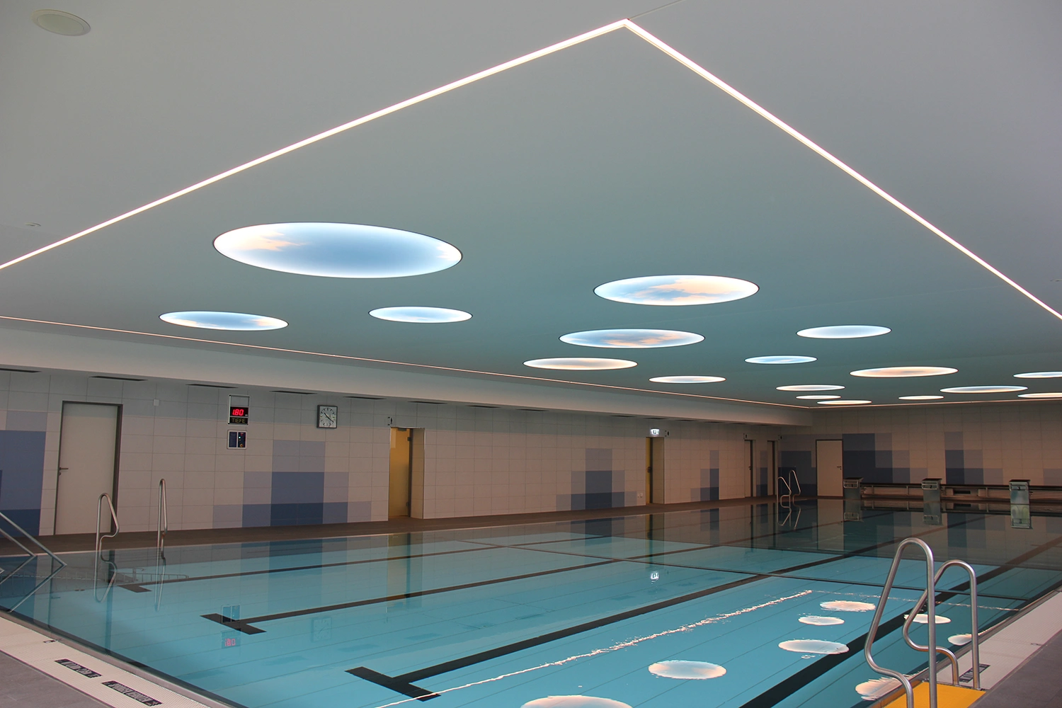 Hallenbad Erolzheim mit klarem blauen Wasser, gefliestem Beckenrand und moderner Decke mit runden Oberlichtern.