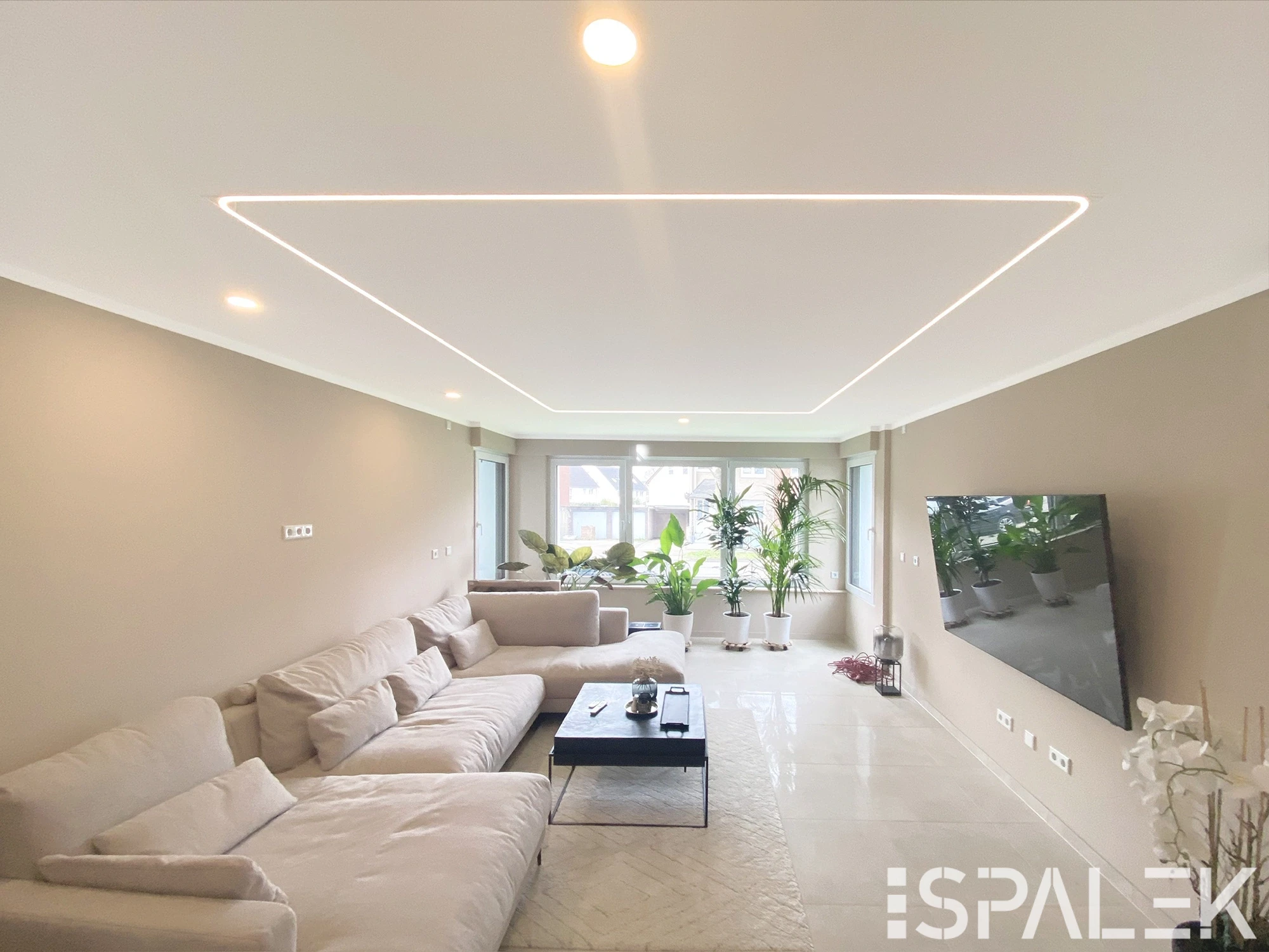 Modernes Wohnzimmer mit beigen Wänden, cremefarbenem Sofa, schwarzem Couchtisch, TV an der Wand und LED-Deckeneinbauleuchten.