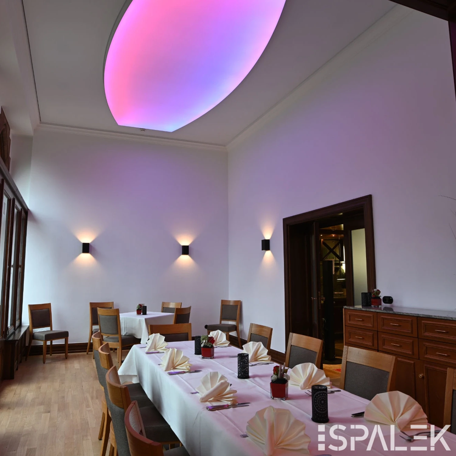 Moderner Speiseraum in Hirschburg mit gedeckten Tischen, Holzstühlen, Wandleuchten und großer Deckenleuchte in Pink und Lila.
