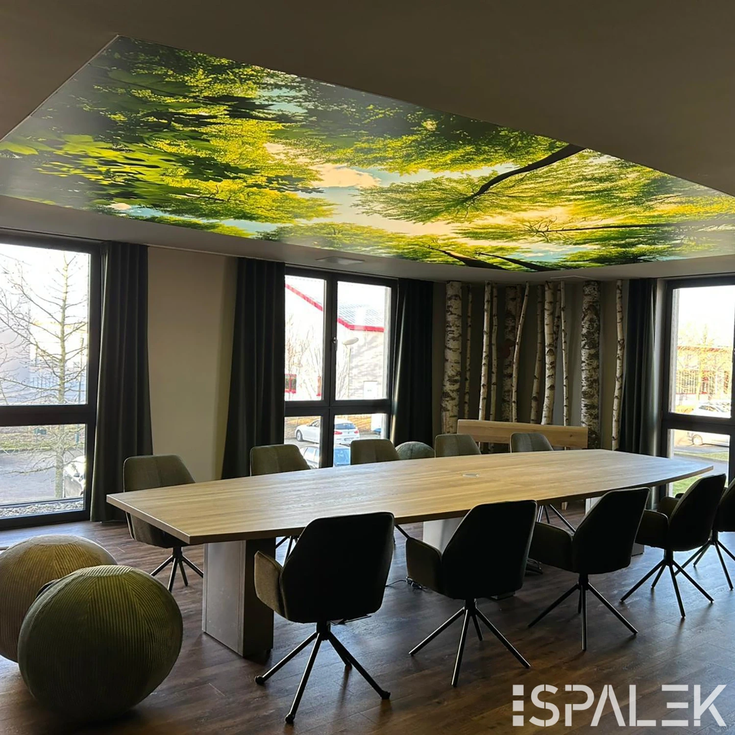 Moderner Besprechungsraum bei Westpress mit langem Holztisch, Drehstühlen, grünen Poufs, großen Fenstern und Naturmotiv-Decke.
