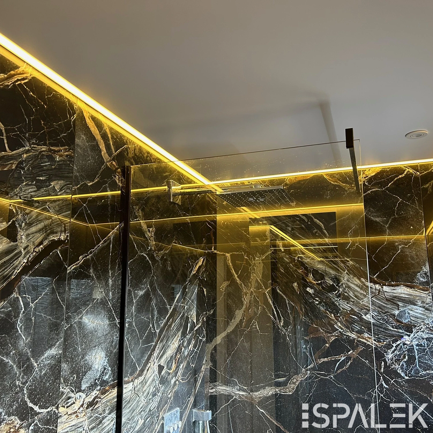 Modernes Badezimmer mit dunklen Marmorwänden, Glasdusche und gelbem LED-Lichtband entlang der Motivdecke.