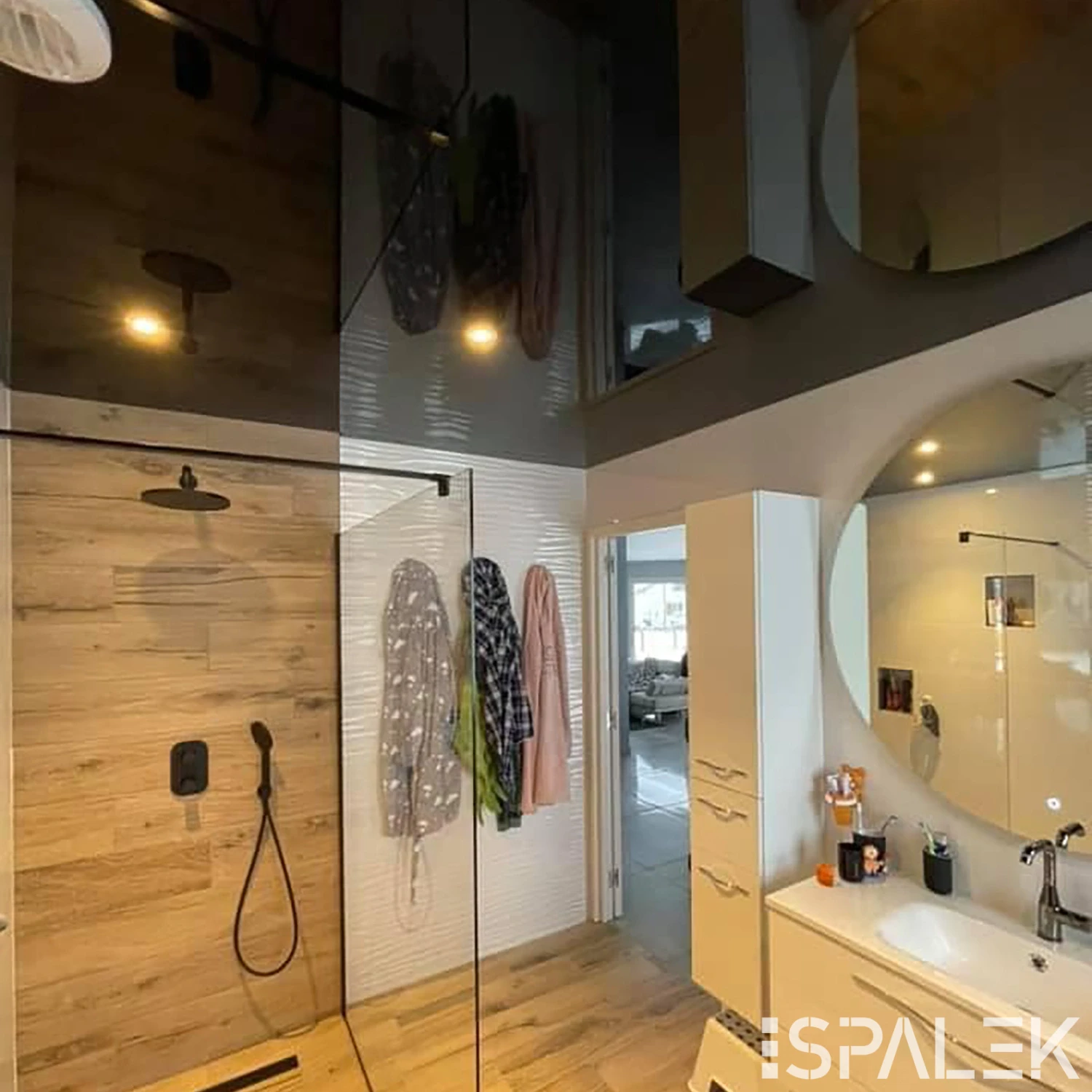 Modernes Badezimmer mit Glasdusche, Holzverkleidung, zwei runden Spiegeln und glänzender Decke mit Lichtreflexen.