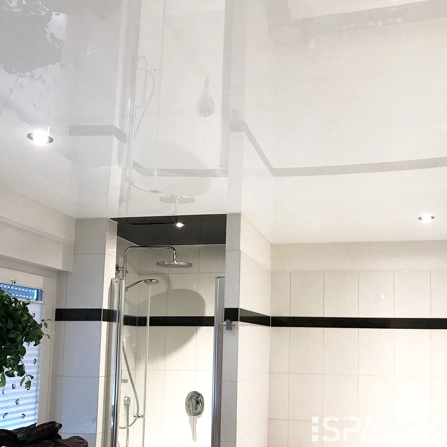 Modernes Badezimmer mit weißen Fliesen, einer Glasdusche und einer glänzenden Decke, die Spots und Beleuchtung reflektiert.