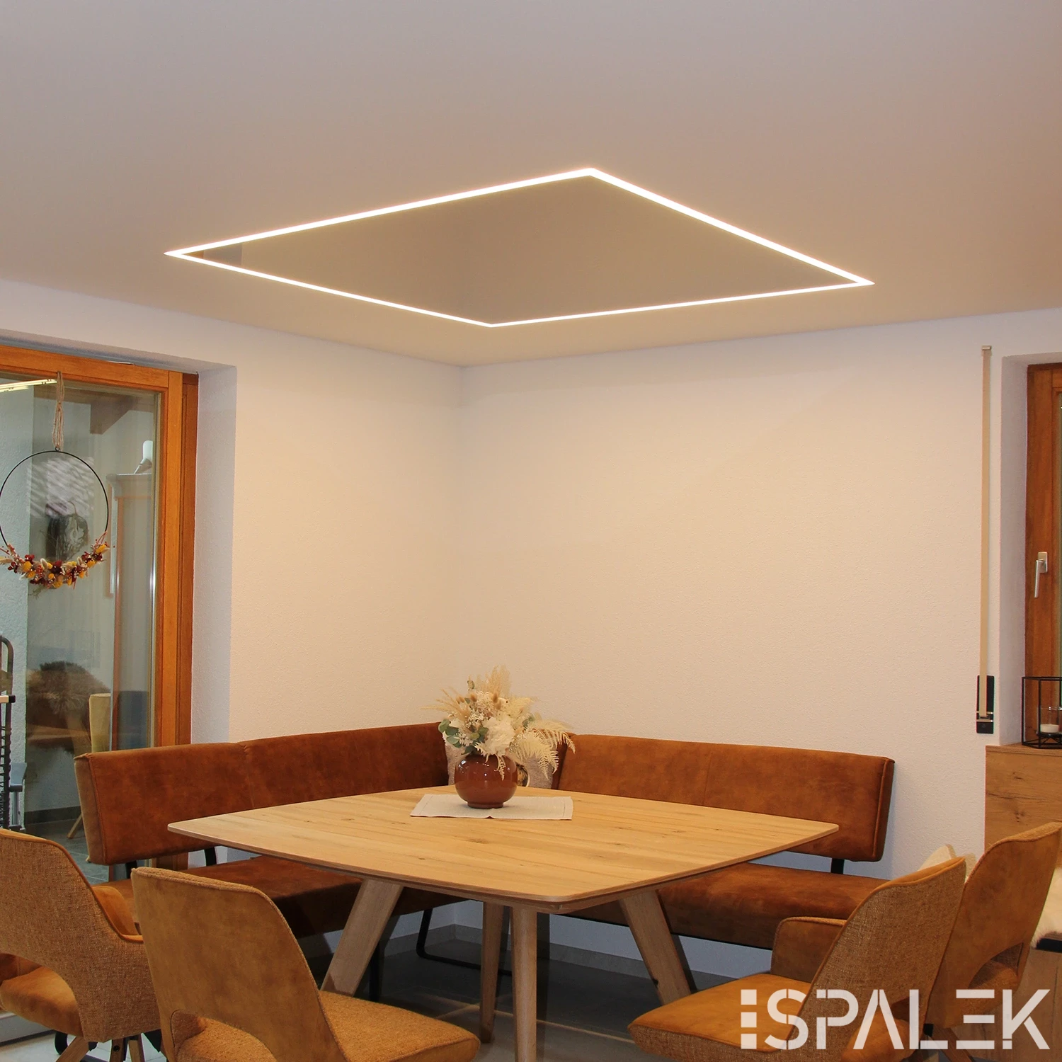 Moderner, weiß glänzender Essbereich mit Holztisch, braunen Polsterstühlen, Eckbank und quadratischer LED-Hängelampe.