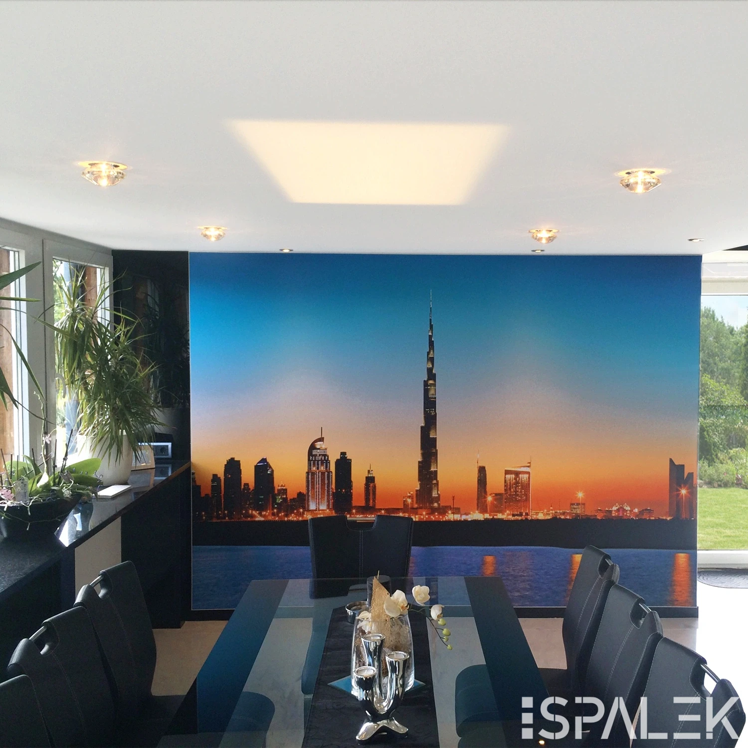Moderner Essbereich mit weißem Glastisch, schwarzen Stühlen und Hängelampe. Wandbild Dubai Skyline, Fenster mit Blick ins Grüne.