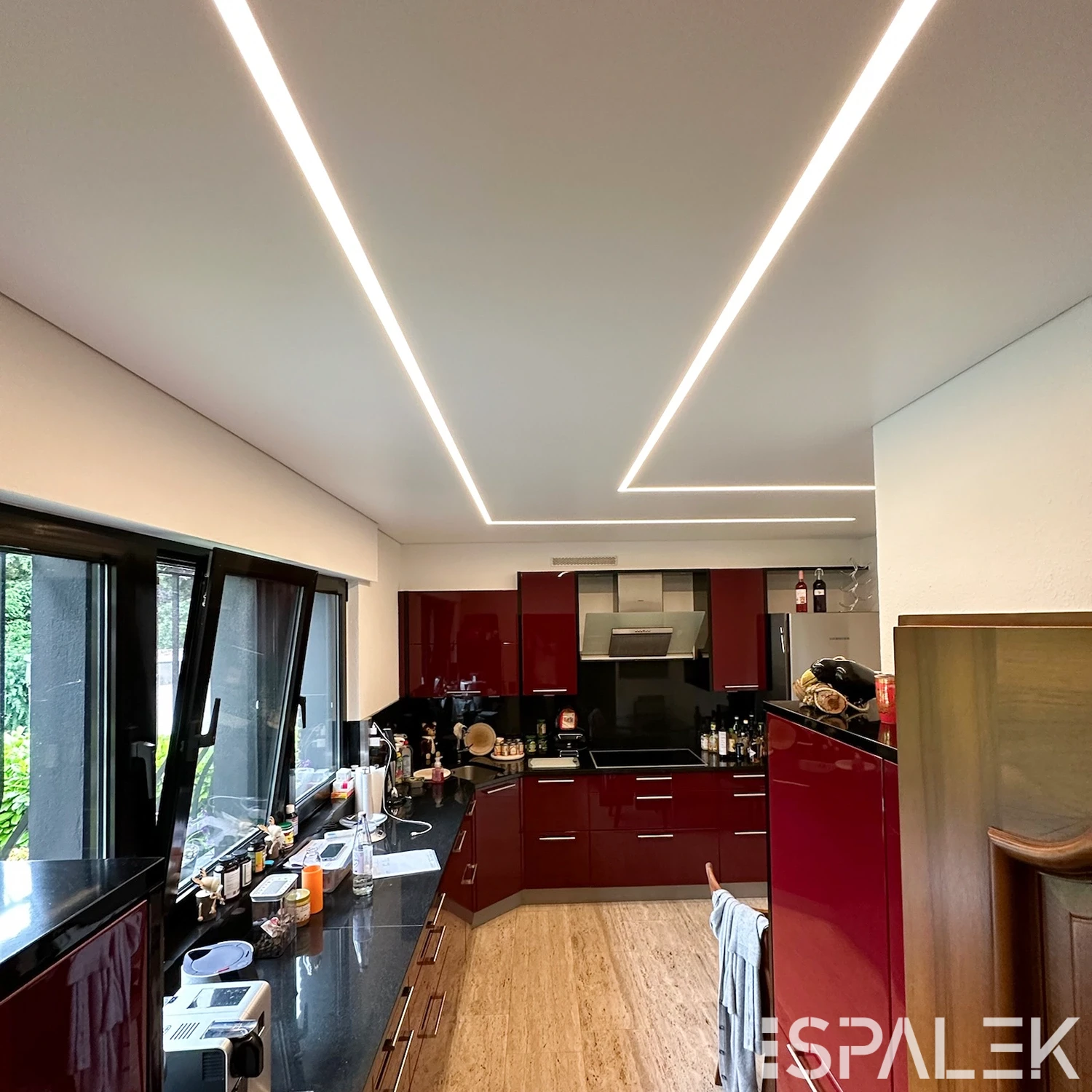 Moderne weiße Küche mit seidenmatten, roten Hochglanzfronten, schwarzen Arbeitsplatten und Einbaugeräten. LED-Deckenleuchten.