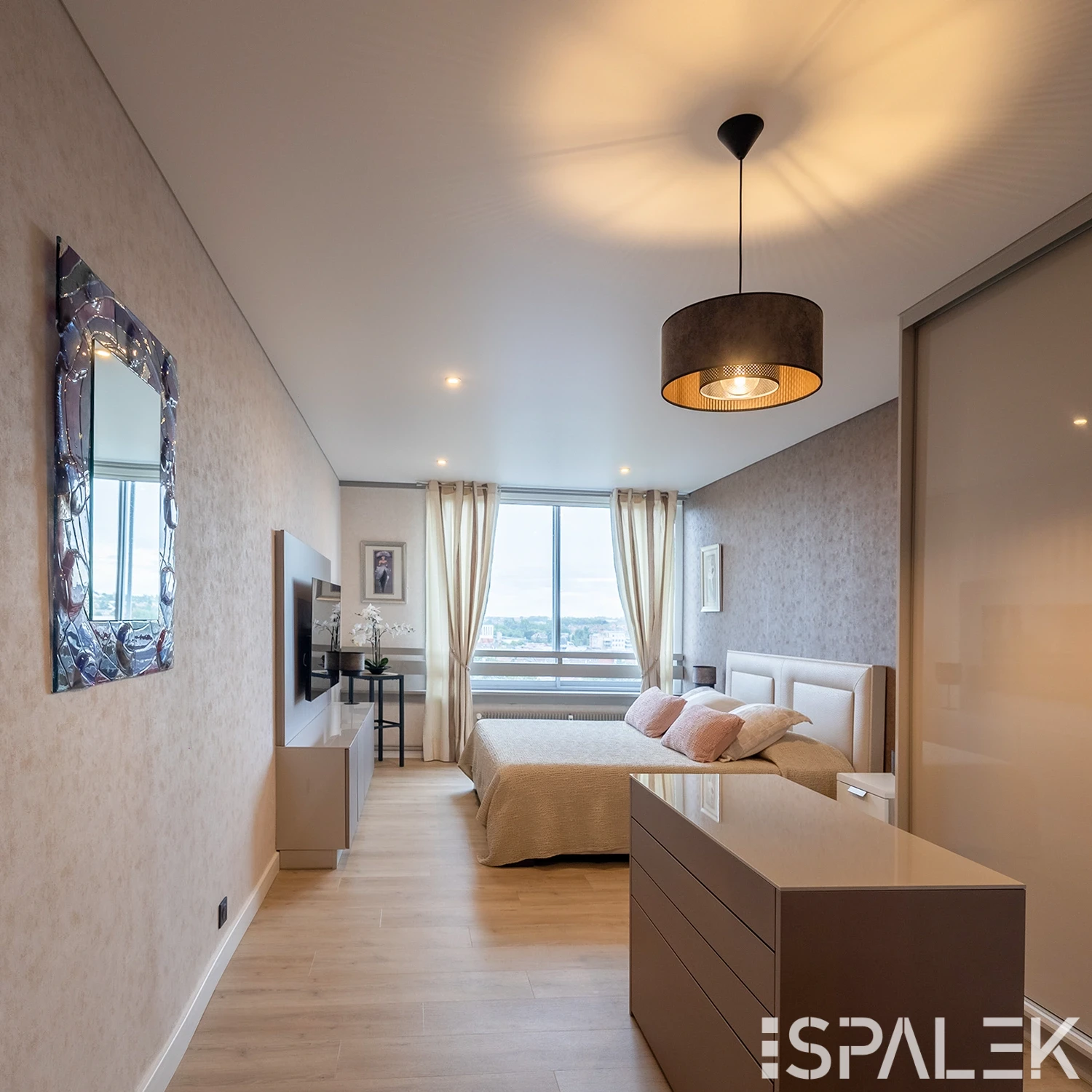 Modernes, weiß glänzendes Schlafzimmer mit großem Fenster, beigen Wänden, Doppelbett mit pinken Kissen und schlichter Einrichtung.