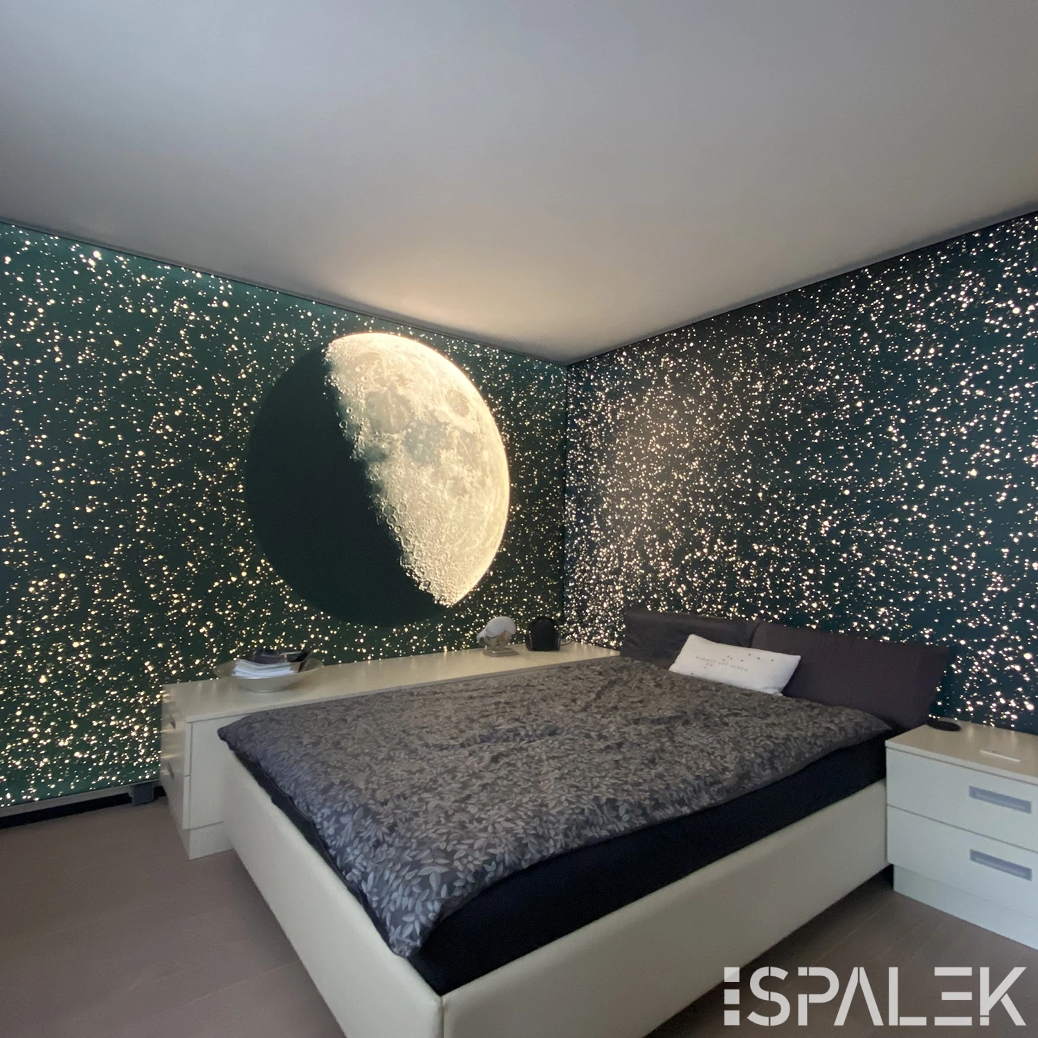 Modernes Schlafzimmer mit großem Mondmotiv und sternförmigen Lichtern an dunkelgrünen Wänden, graues Doppelbett, weiße Nachttische.