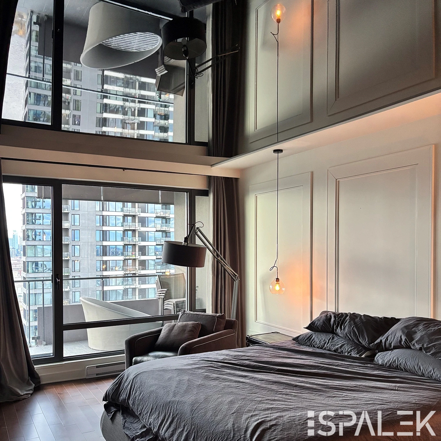 Modernes Schlafzimmer mit grauer Bettwäsche, schwarzem Sessel, Stehlampe, Hängelampen und glänzender weißer Decke.