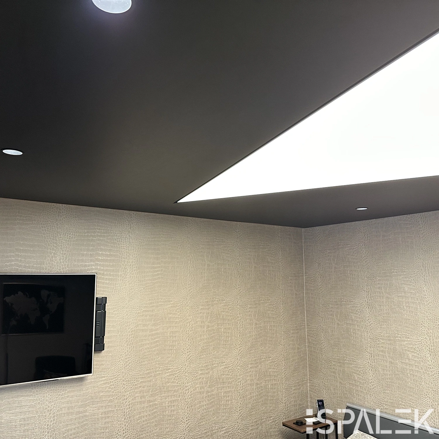 Modernes Schlafzimmer mit strukturierter beiger Wand, Wand-TV, kleinem Schreibtisch und dunkler Decke mit Lichtdecke und Spots.