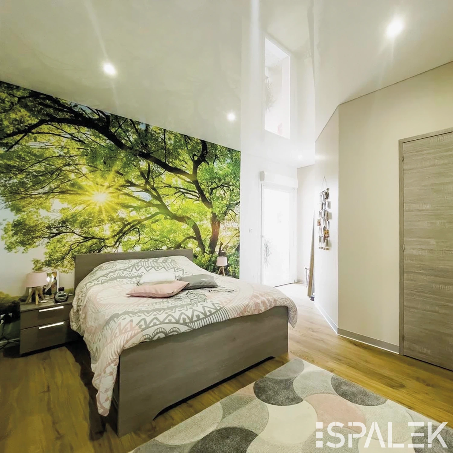 Modernes Schlafzimmer mit Holzbett, Natur-Wandmotiv, weißen Akzenten, Holzfußboden, geometrischem Teppich und viel Tageslicht.