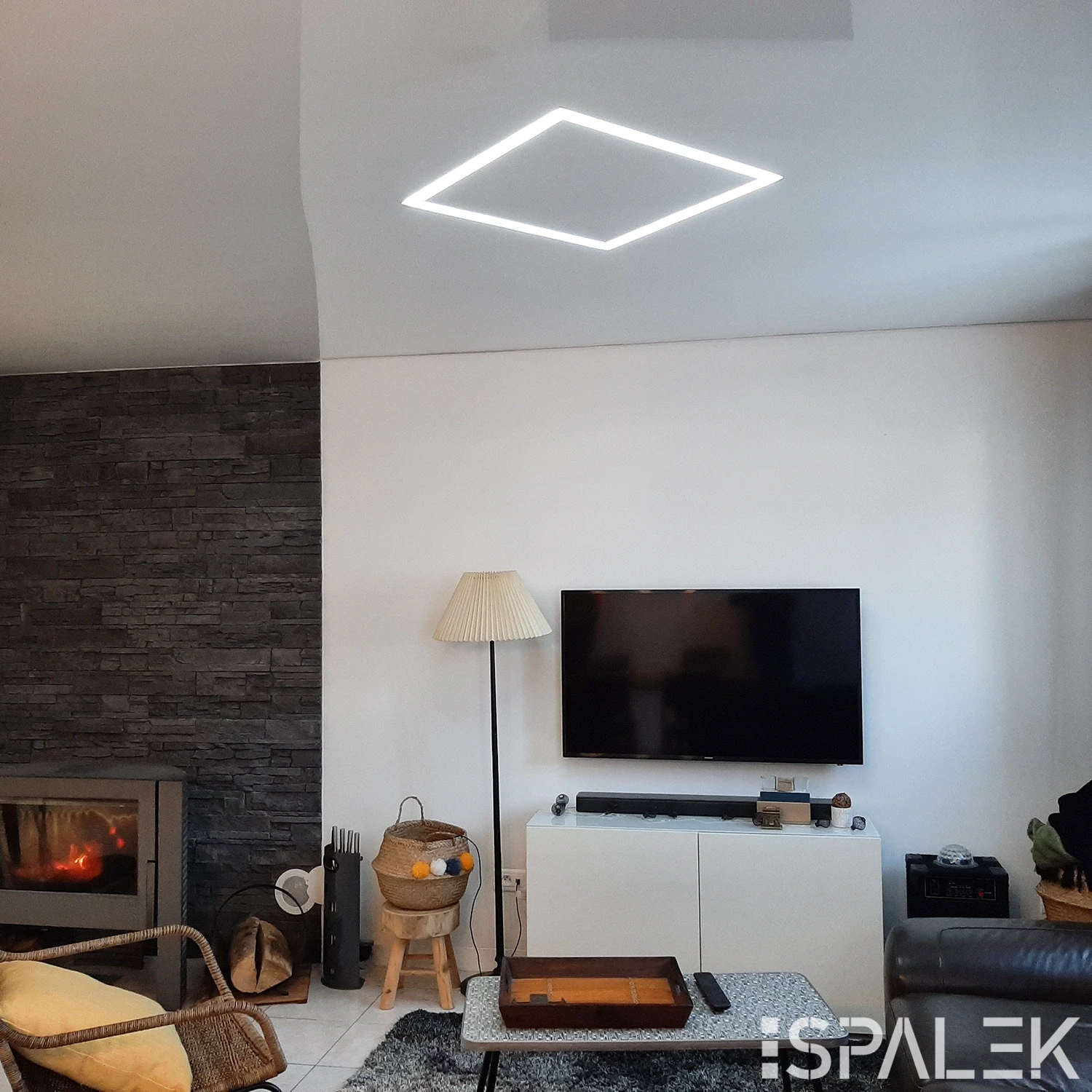 Modernes Wohnzimmer mit wandmontiertem TV, weißem Schrank, Kaminfeuer, quadratischer LED-Lichtleiste und gemütlicher Sitzecke.