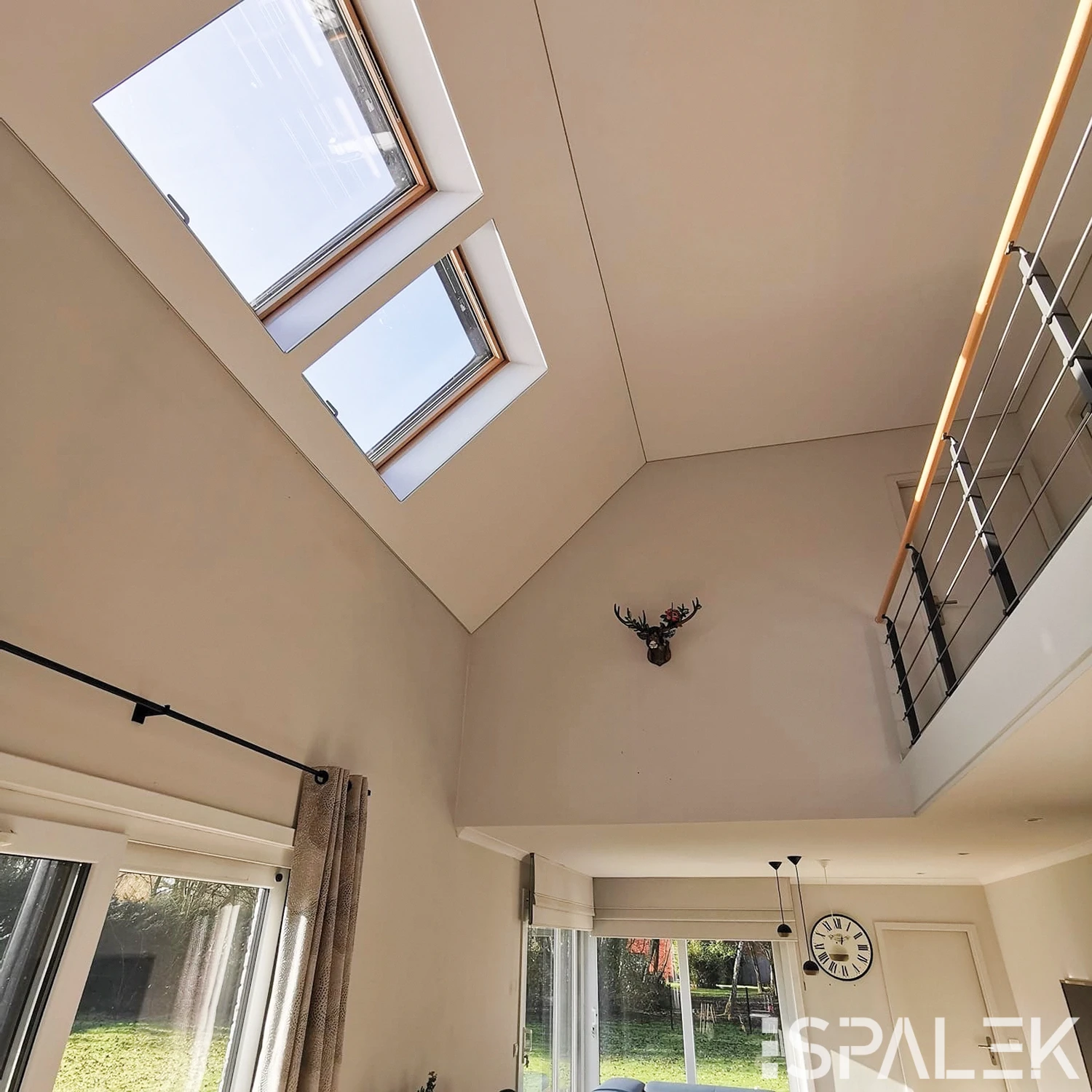 Modernes Wohnzimmer mit hohen Decken, großen Oberlichtern, Hirschkopf-Dekoration, Schiebetüren, Lichtleiste und Uhr über der Tür.