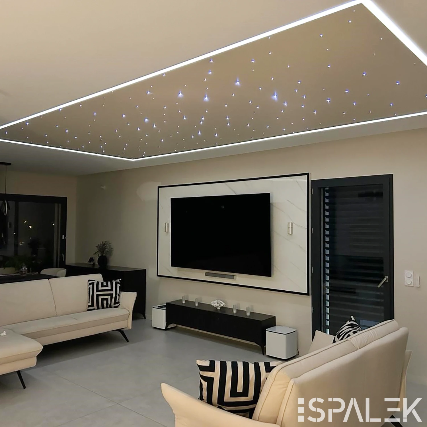 Modernes Wohnzimmer mit weißen Sofas, geometrischen Kissen, großem Wand-TV und Decke mit kleinen LED-Leuchten und Lichtleiste.