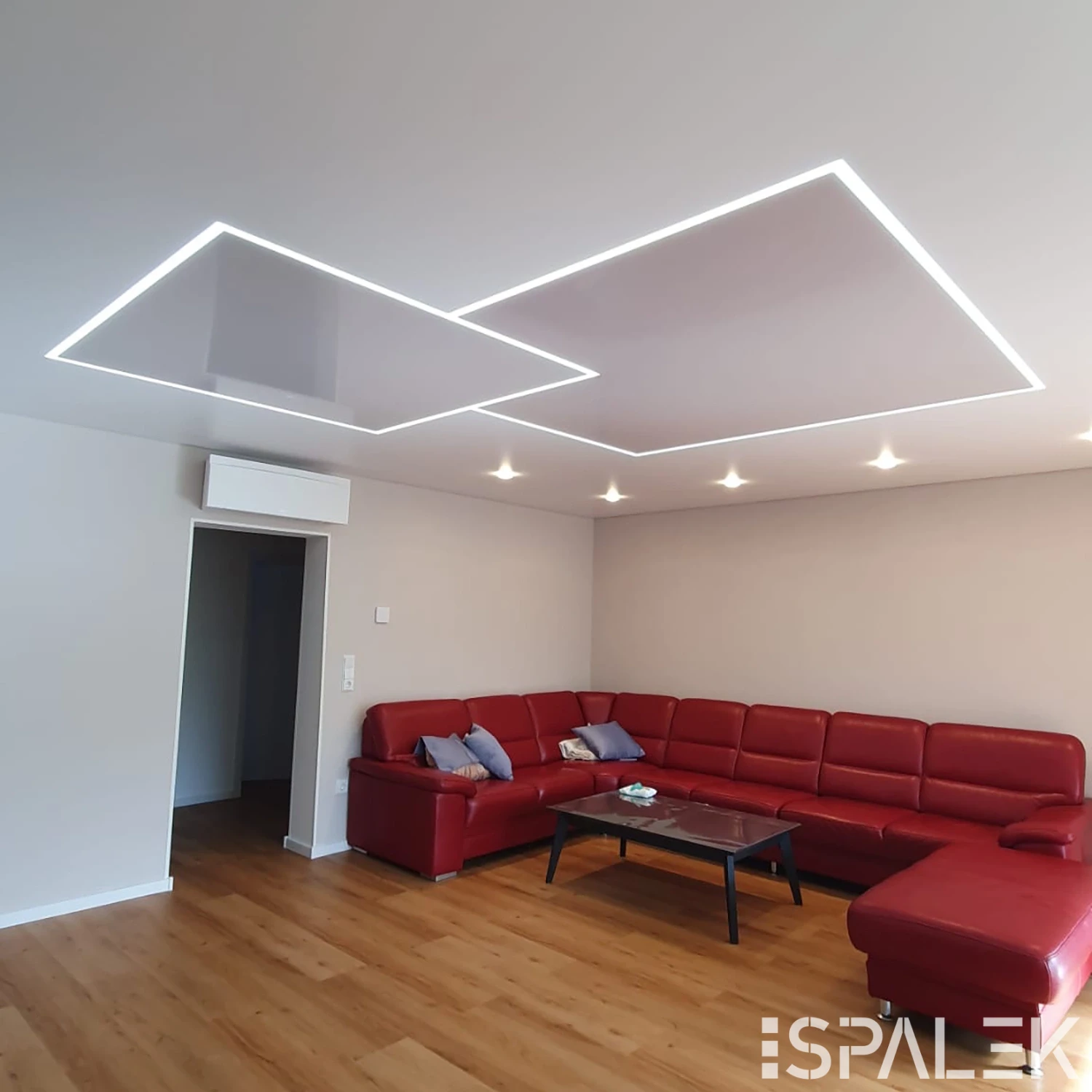 Modernes Wohnzimmer mit großem roten Ecksofa, Holzboden, Glastisch und geometrischen LED-Deckenleuchten mit Lichtleiste.