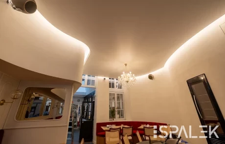 Das stilvolle Restaurant Brasserie Dufour mit geschwungenen weißen Wänden, warmem Licht, roten Polsterbänken und Holzmöbeln.
