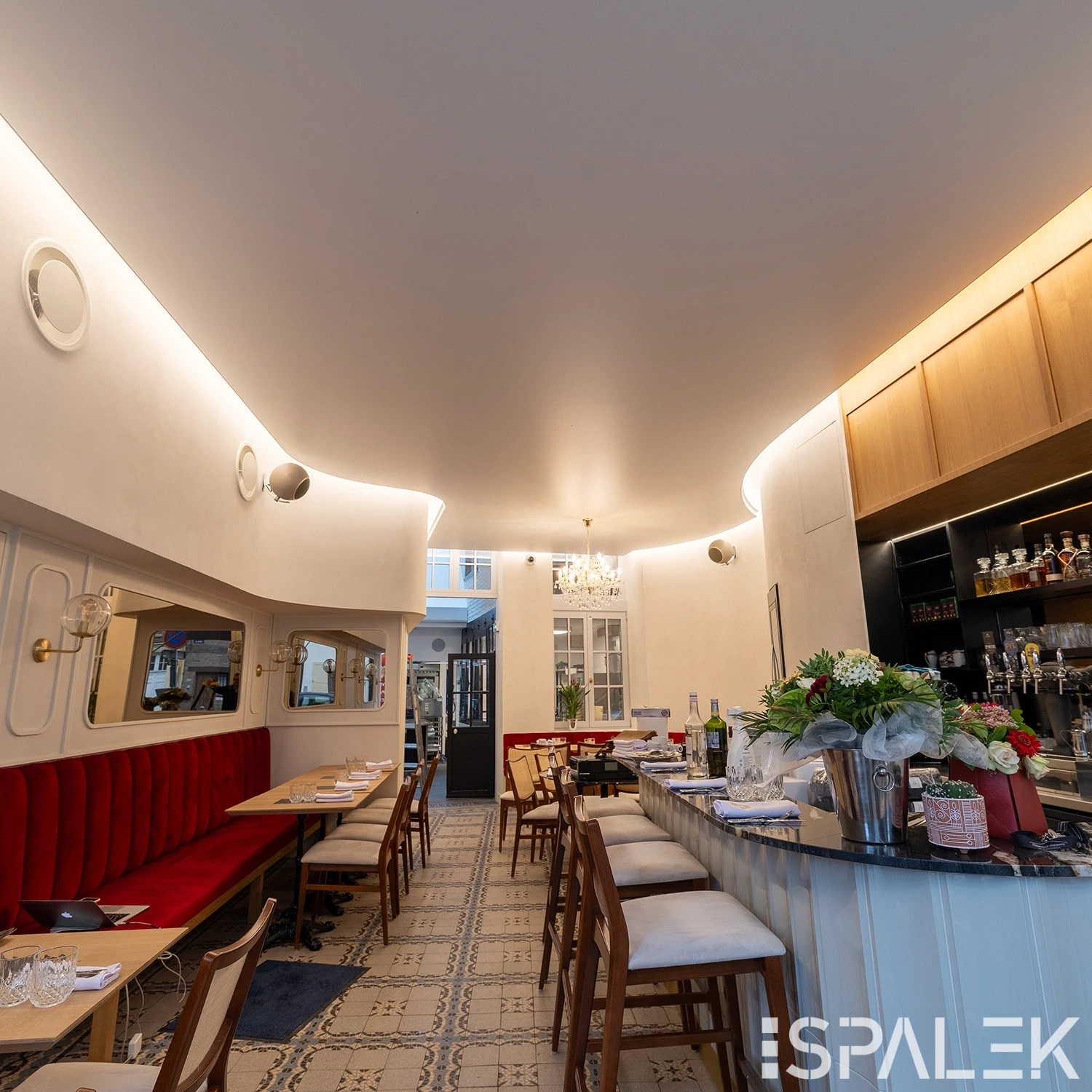 Modernes, elegantes Brasserie Dufour Interieur mit gebogener Decke, roten Samtbänken links, Holzbänken an Marmortischen und heller Bar rechts.