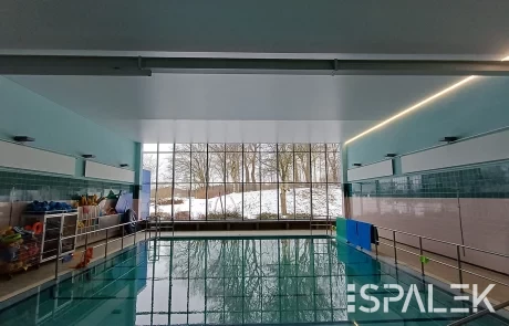 Hallenbad mit türkisfarbenen Fliesen und Geländern im Schwimmbad Raisdorf, großes Fenster mit Blick auf verschneite Bäume.