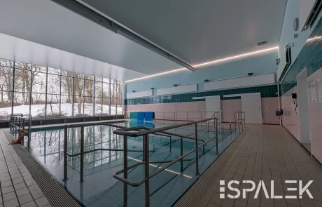 Das Therapiebecken im DRK Schwimmbad Raisdorf mit Edelstahlgeländern, Fliesenboden und großen Fenstern zu verschneiten Bäumen.