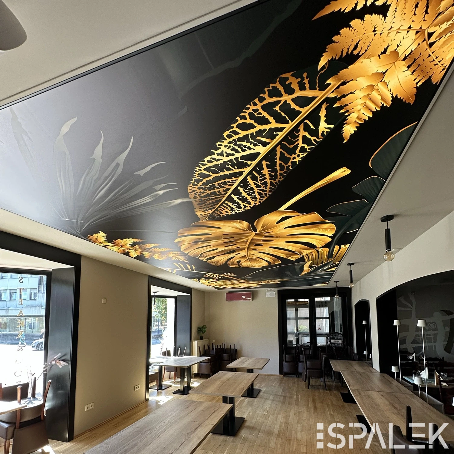 Modernes Restaurant mit holzigen, hellen Holzböden und großen Fenstern; Deckenmotiv aus goldenen Blättern auf dunklem Grund.