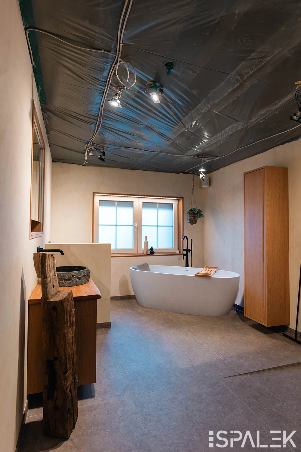 Modernes Bad mit freistehender weißer Wanne, Holzmöbeln, Steinwaschbecken, Baumstammdetails und großem Fenster. Unfertige Decke.