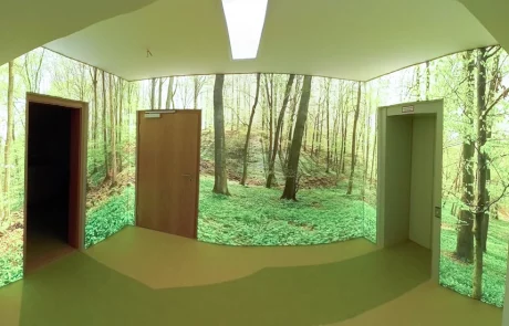 Ein Flur mit zwei Türen und einem Aufzug, dessen Wände ein raumhohes, realistisches Waldmotiv schmückt. SPALEK-Logo unten rechts.