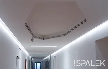 Weißer Flur mit Türen beidseitig, hexagonalem Deckenausschnitt und moderner LED-Beleuchtung; Fenster am Ende. ESPALEK Logo unten rechts.