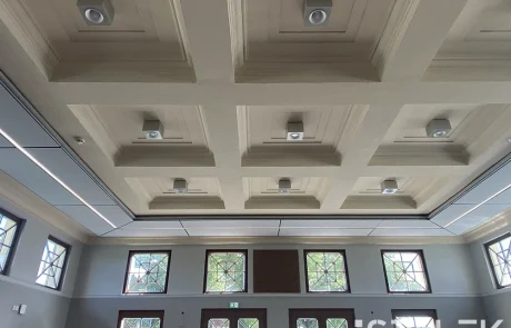 Seminar24fertig1 Decke eines modernen Raums mit quadratischen, abgesetzten Feldern, integrierter Beleuchtung und großen rechteckigen Fenstern mit Gittermuster an den Wänden; ruhige Atmosphäre, als befände man sich mitten im Wald.